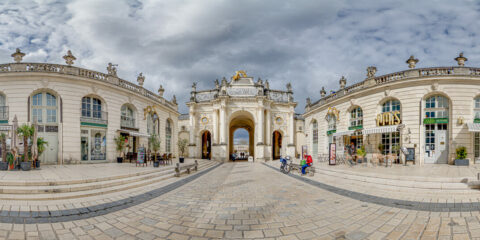 Arc monumental sur une place pavée, ciel nuageux.
