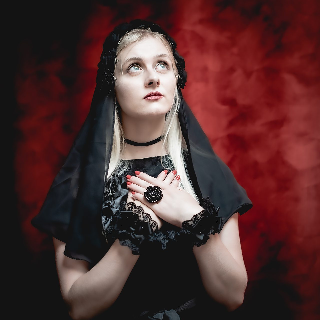 Femme en robe noire sur fond rouge, mains croisées.