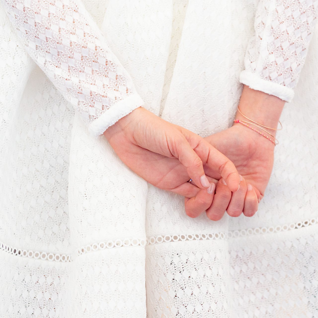 Mains croisées, robe blanche en dentelle.