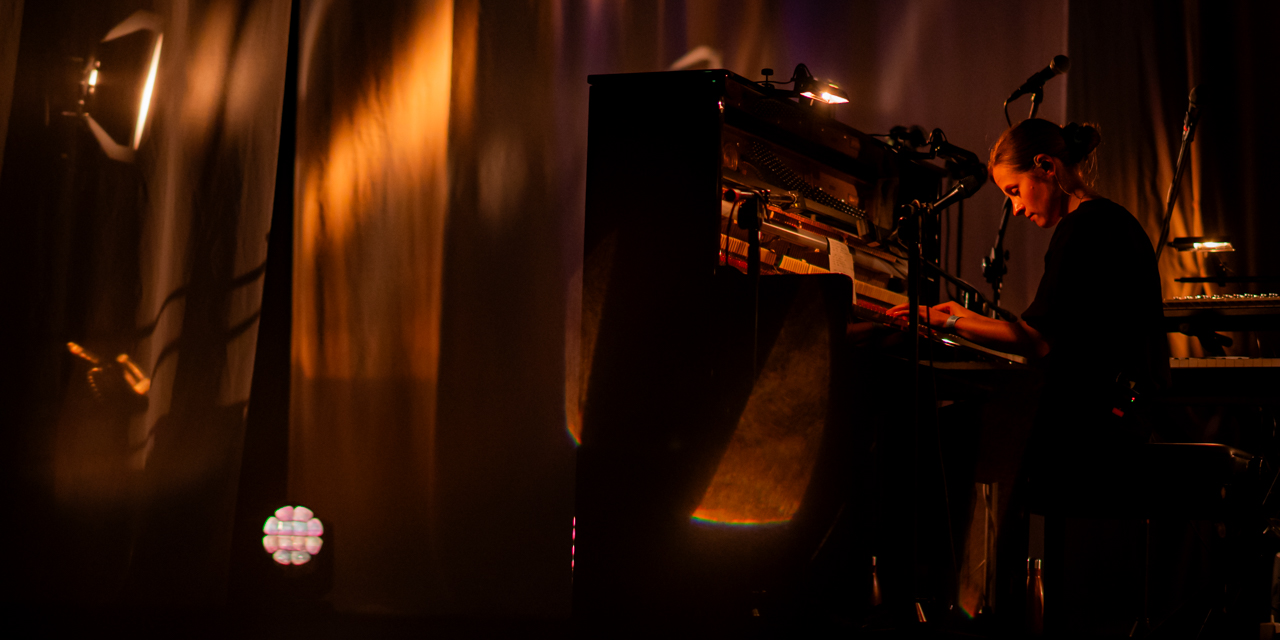 Musicienne jouant du piano sur scène éclairée.