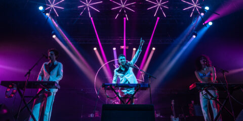 Concert avec lumières violettes et artistes sur scène.