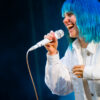 Personne chantant sur scène, cheveux bleus fluorescent.