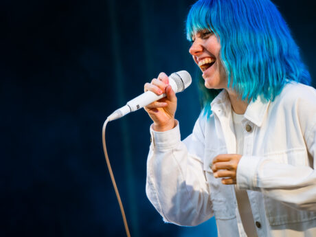 Personne chantant sur scène, cheveux bleus fluorescent.