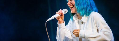 Personne chantant sur scène, cheveux bleus fluorescent.