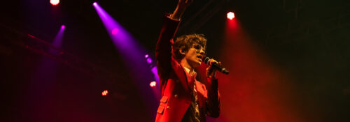 Chanteur sur scène avec micro et lumières colorées.