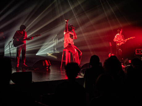Groupe musical en concert, éclairages rouges et blancs.