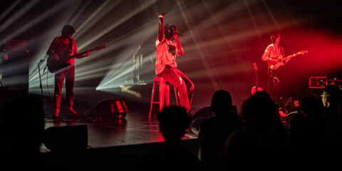 Groupe musical en concert, éclairages rouges et blancs.