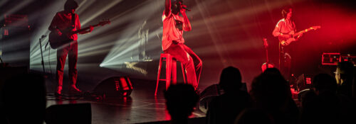 Groupe musical en concert, éclairages rouges et blancs.