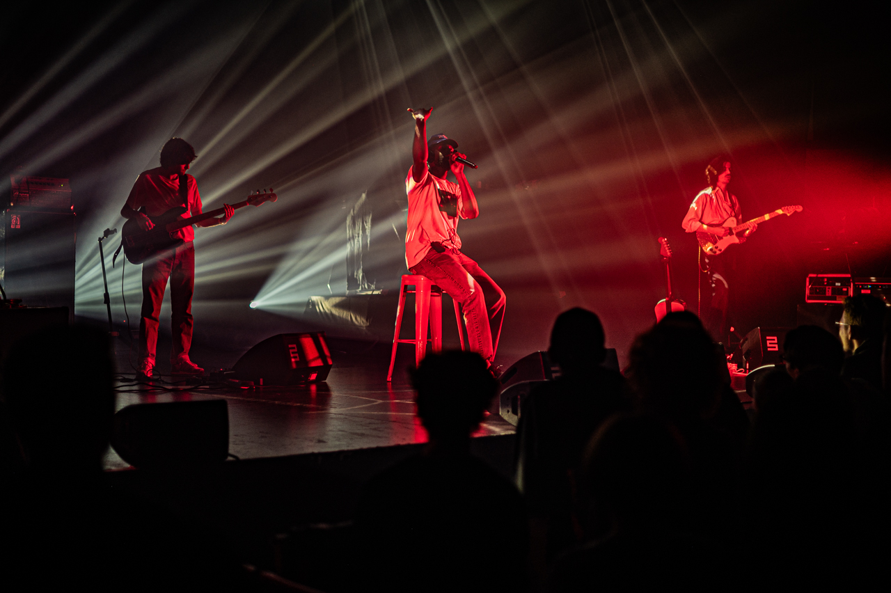 Groupe musical en concert, éclairages rouges et blancs.