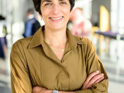 Personne souriante en chemise marron, bras croisés.