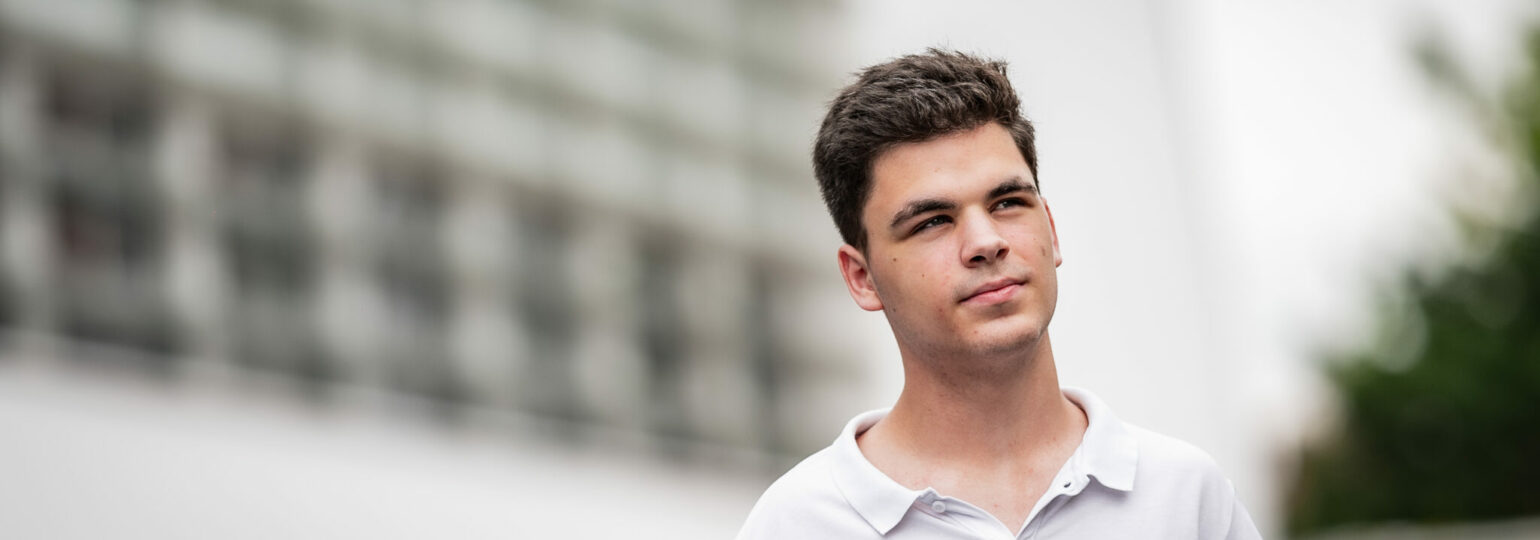 Jeune homme pensif en extérieur urbain flou.