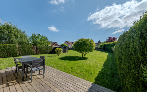 Jardin vert avec terrasse en bois et mobilier.