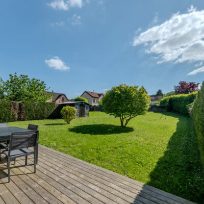 Jardin vert avec terrasse en bois et mobilier.