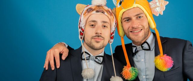 Deux hommes en costumes avec bonnets animaux colorés.