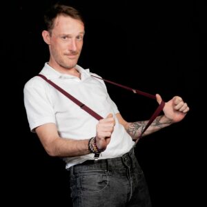 Homme avec bretelles souriant sur fond noir.