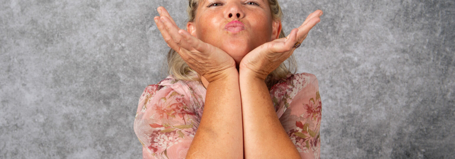Femme souriante envoie un bisou devant un fond gris.