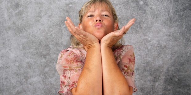 Femme souriante envoie un bisou devant un fond gris.