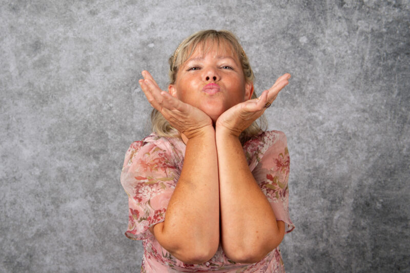 Femme souriante envoie un bisou devant un fond gris.