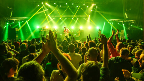 Concert animé avec foule enthousiaste sous lumières vertes.