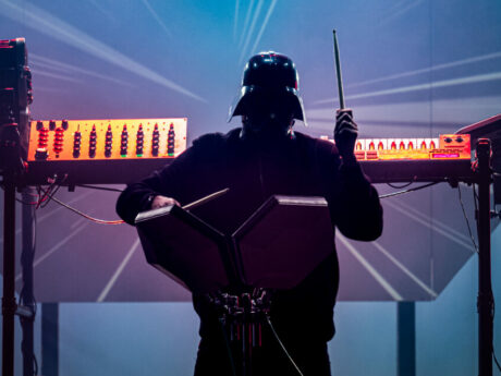 Musicien masqué jouant des percussions électroniques sur scène.