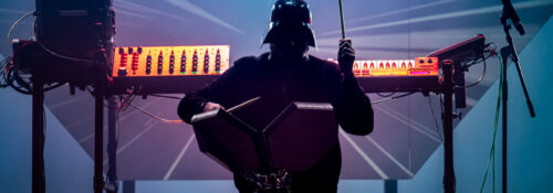 Musicien masqué jouant des percussions électroniques sur scène.