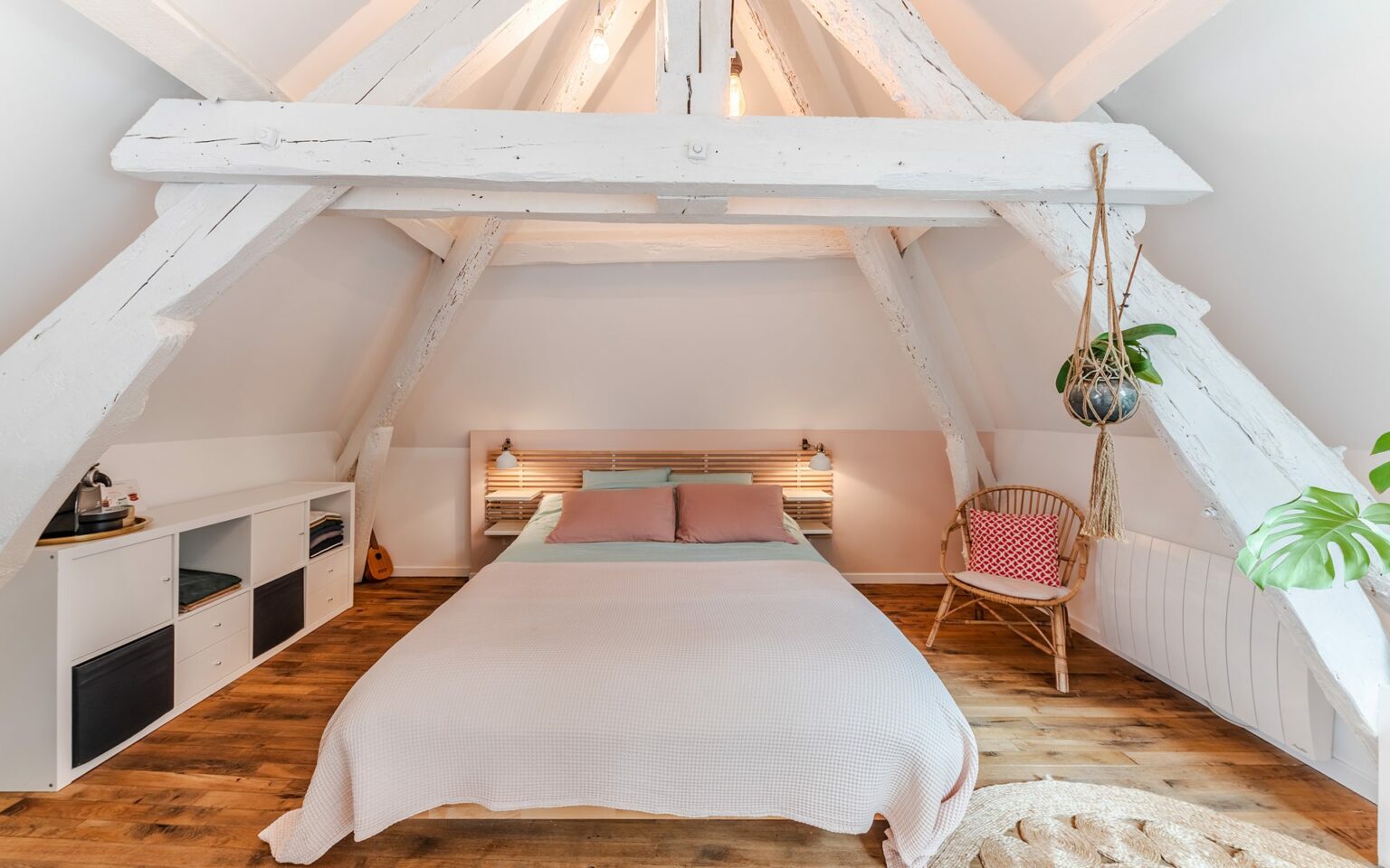 Chambre sous combles avec lit et plantes suspendues.