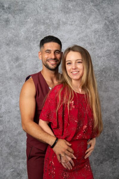 Couple souriant en tenue rouge devant fond gris.