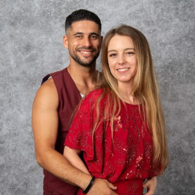 Couple souriant en tenue rouge devant fond gris.