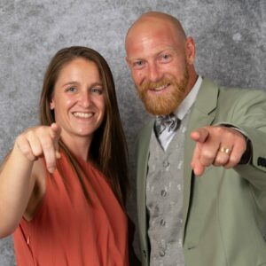 Deux personnes souriantes pointent vers l'objectif.