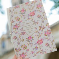 Faire-part de baptême fleuri tenu en main.