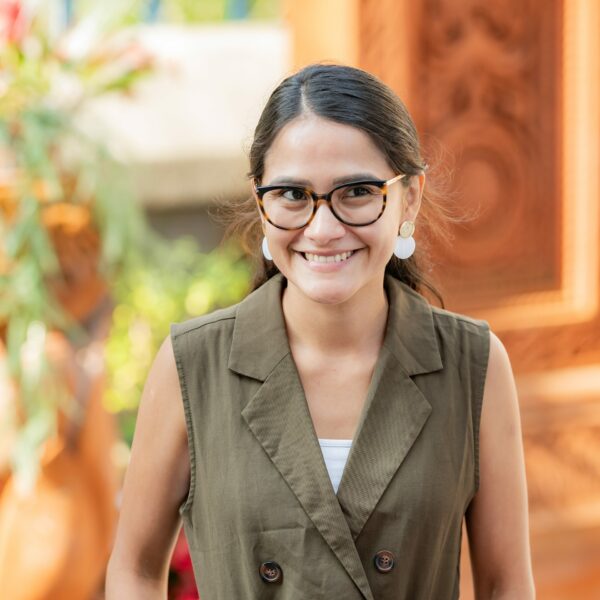 Femme souriante portant des lunettes et une veste kaki.