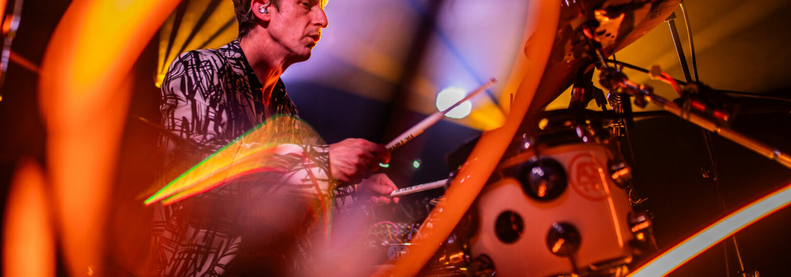 Batteur jouant sur scène sous éclairage coloré.
