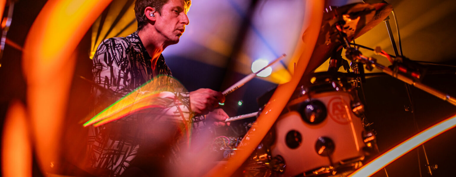 Batteur jouant sur scène sous éclairage coloré.