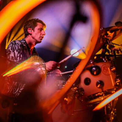 Batteur jouant sur scène sous éclairage coloré.