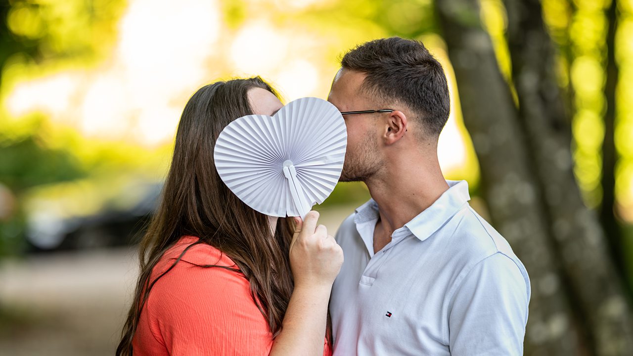 Couple cachant un baiser avec éventail cœur.