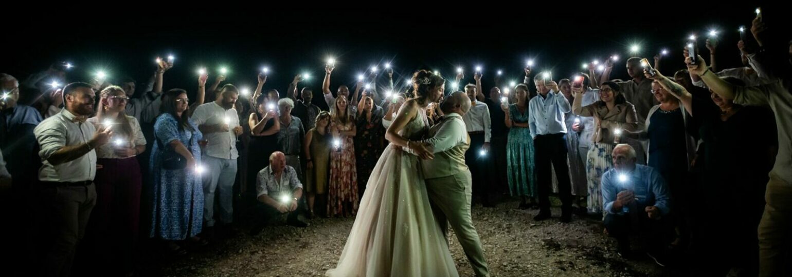 Mariage de nuit entouré d'invités avec téléphones illuminés.