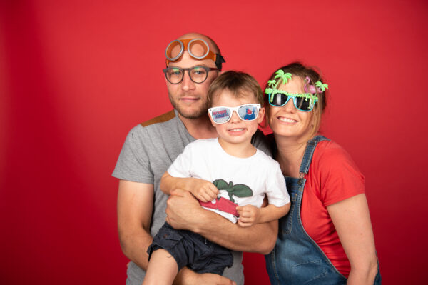 Famille souriante avec lunettes amusantes, fond rouge.