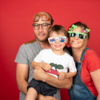 Famille souriante avec lunettes amusantes, fond rouge.