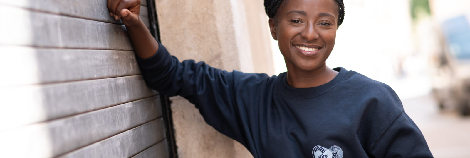 Personne souriante appuyée contre un mur métallique.