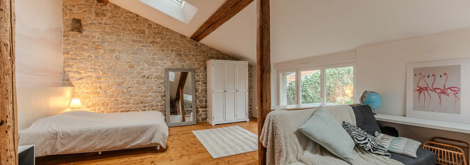 Chambre mansardée avec pierres apparentes et fenêtres de toit.