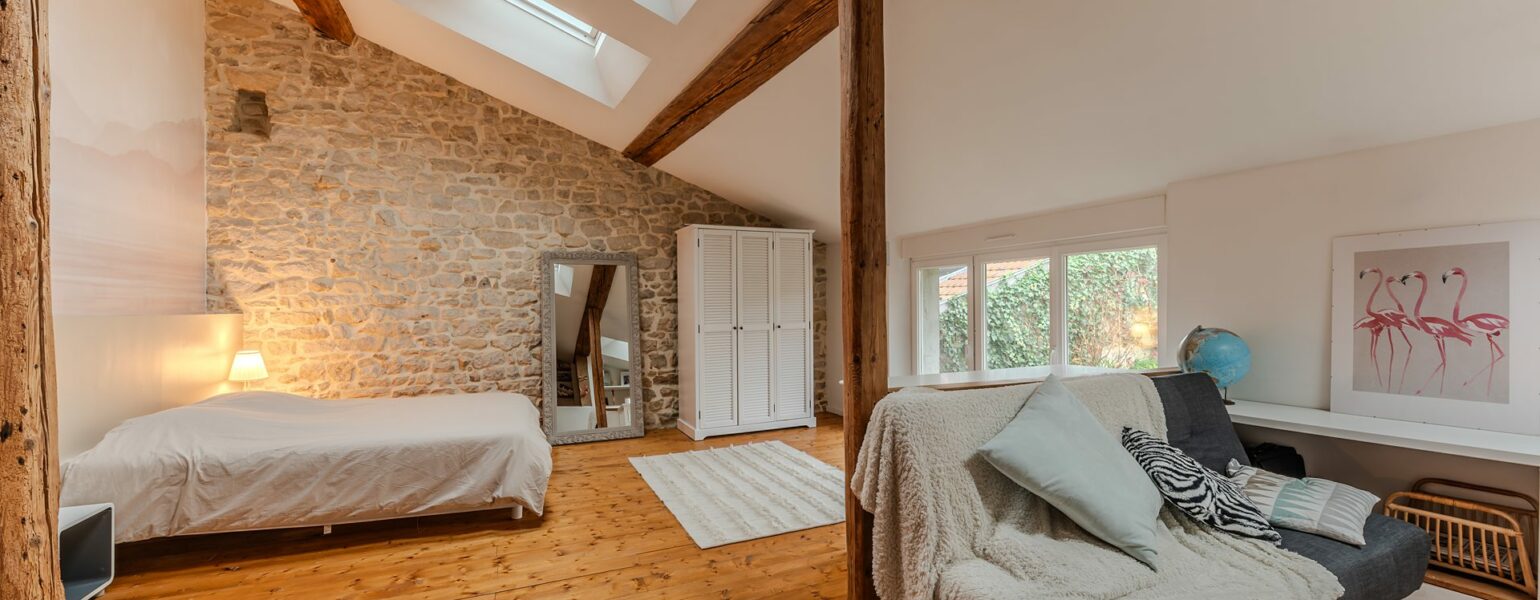 Chambre mansardée avec pierres apparentes et fenêtres de toit.