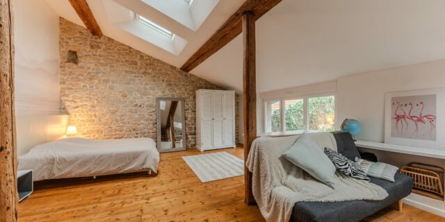 Chambre mansardée avec pierres apparentes et fenêtres de toit.