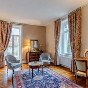 Salon élégant avec meubles anciens et tapis coloré.