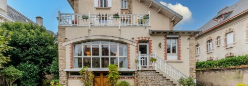 Maison en briques avec jardin, ciel bleu.