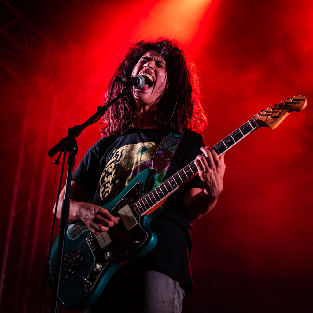 Chanteur sur scène avec guitare et éclairage rouge.