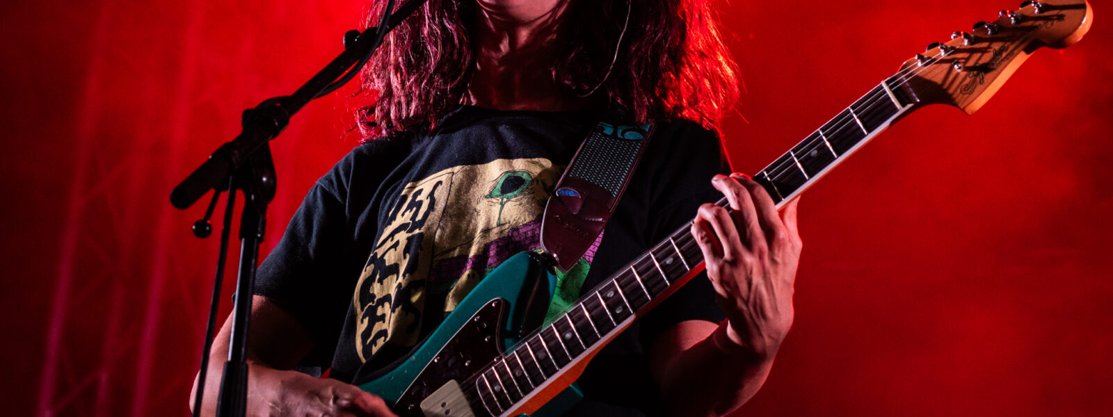 Chanteur sur scène avec guitare et éclairage rouge.