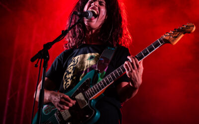 Chanteur sur scène avec guitare et éclairage rouge.