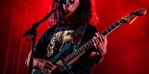 Chanteur sur scène avec guitare et éclairage rouge.