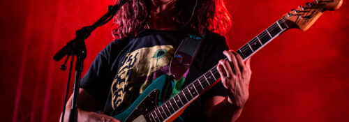 Chanteur sur scène avec guitare et éclairage rouge.