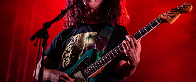 Chanteur sur scène avec guitare et éclairage rouge.